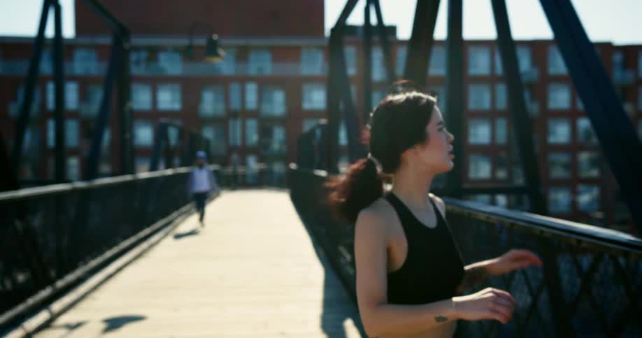 Young woman jogs on a pedestrian bridge near a residential building over train tracks