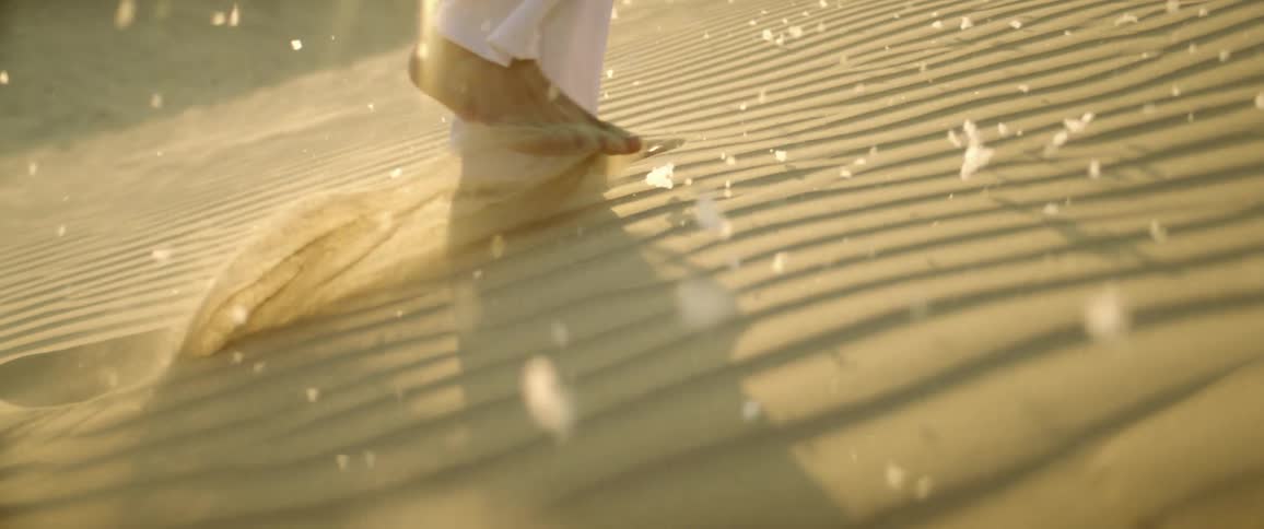 A man walks barefoot in a desert at sunset