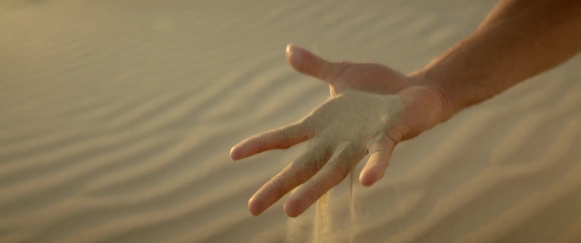 Sand filters through a person's hand in the desert