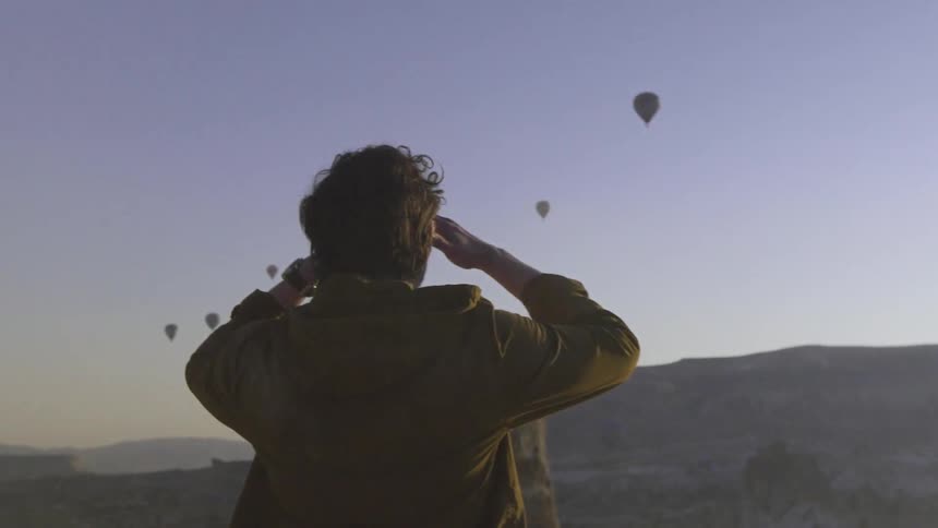 A man is looking up at the sky full of hot air balloons