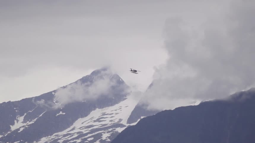 A plane flies over a snow covered mountain on a cloudy day