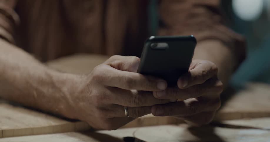Male resting arms on table while holding a smart phone and typing quickly