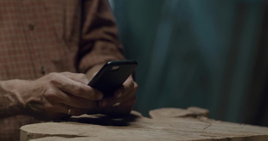 Man texts on mobile phone standing over in progress wood carving