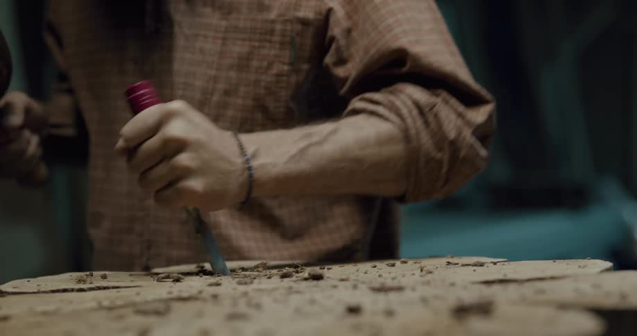 A middle aged man uses a hammer and chisel to carve a tree stump