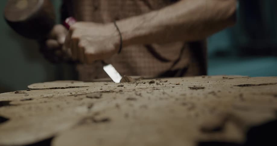 A male using a chisel and a hammer to carve into wood