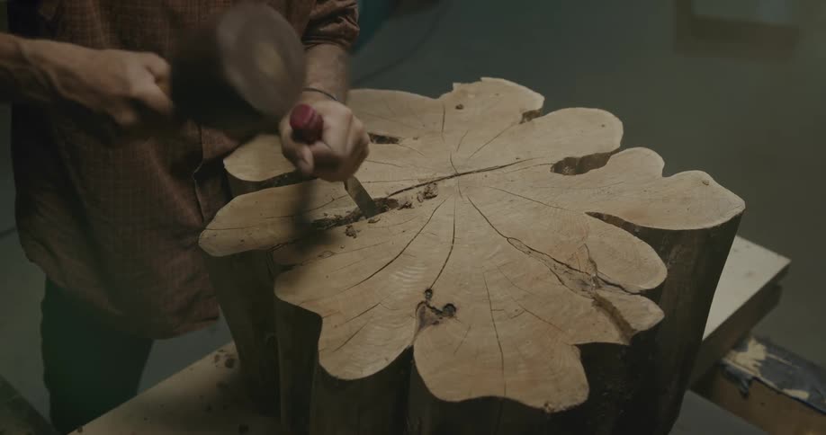 Man carved wooden piece using mallet and chisel in workshop