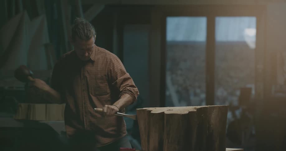 A man with a hammer and chisel sculpting a piece of wood