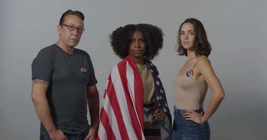 Black woman with an american flag around her shoulders stands between a caucasian woman and man