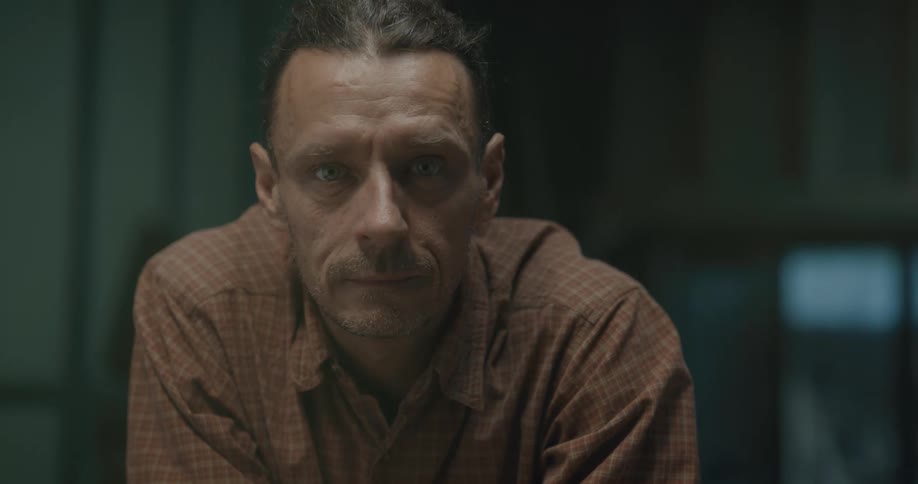 A middle aged man in a plaid shirt raises his head to look into the camera