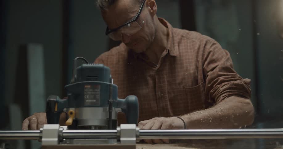 A man wears goggles to protect his eyes from sawdust while sanding a bundle of tree stumps