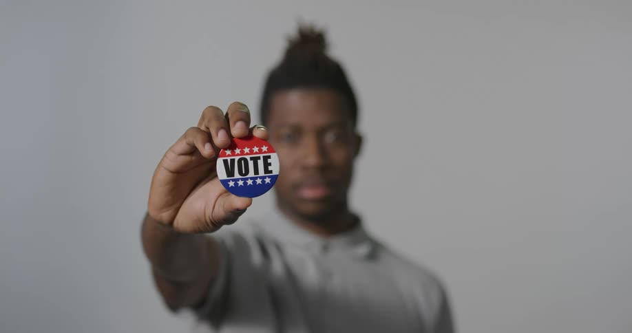 A young black male extends his arm and holds out a pin that reads vote