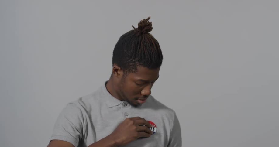 A man with a vote sticker holding it on his hand and putting it on his shirt