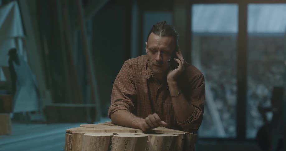 A man talks on the phone as he taps on a wood table