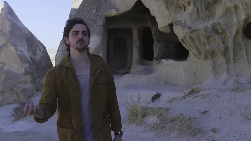 A man standing in a barren landscape walks ahead and closes the compass in his hands