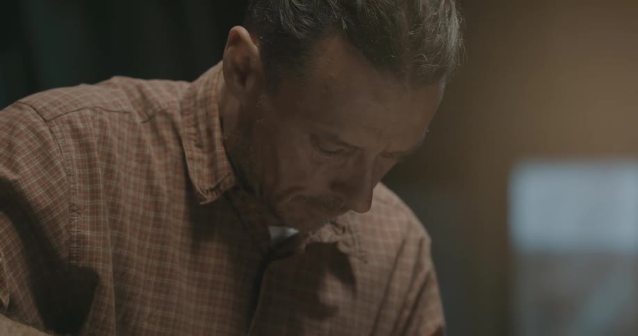 A man with a shirt looking downward with windows in the background