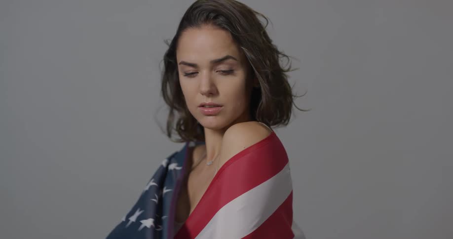 A young woman with dark hair holds an american flag up and wraps it around her shoulders