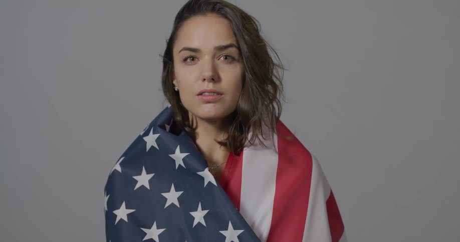 A teen put the american flag over her shoulders and poses for a photo