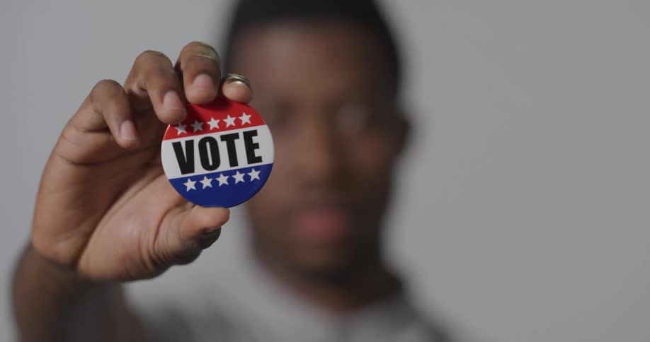 Young man holds a voting pin in front of the camera