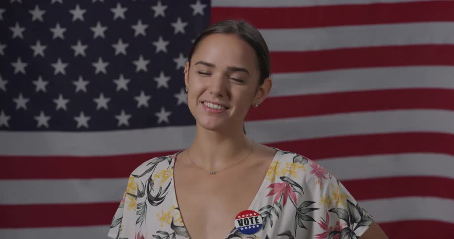 A woman standing in front of the american flag smiles for a photo