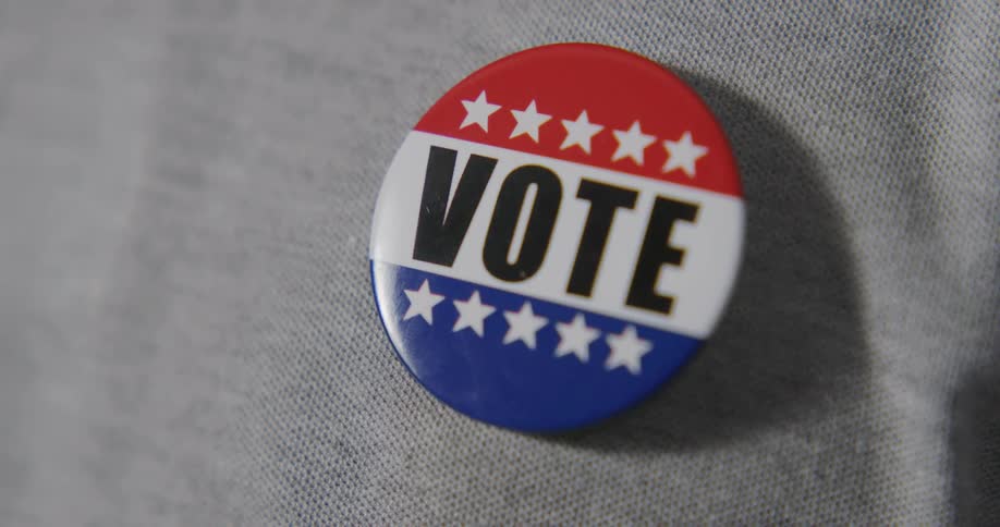 A persons hand putting a vote button on their clothing with light and shadow