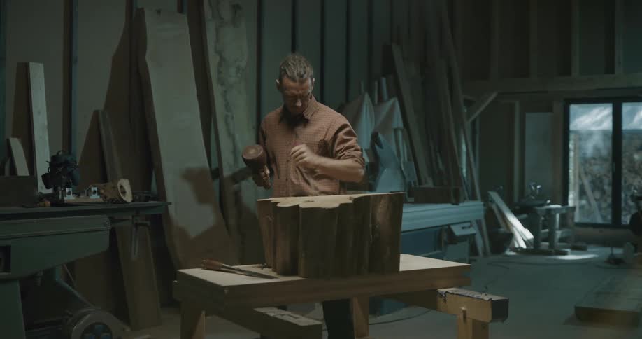 Man carves some wood by pounding a chisel with a hammer in a workshop