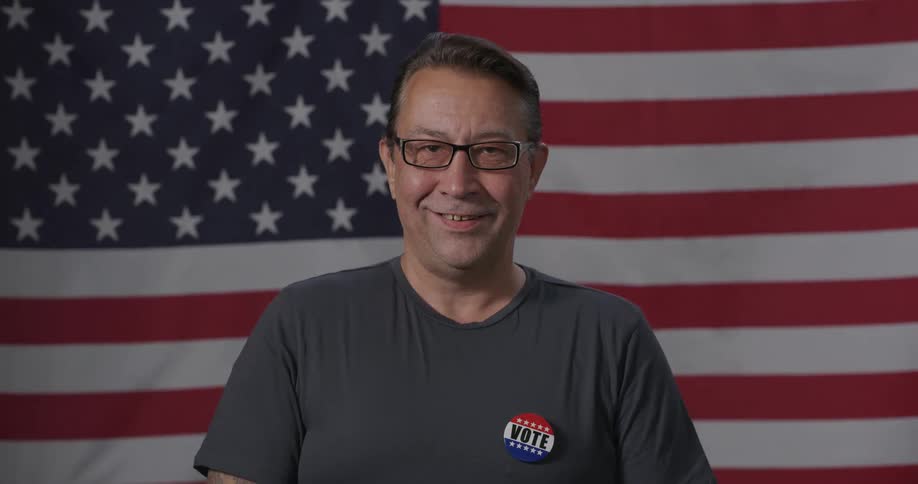 Smiling man posing in front of the american flag after voting