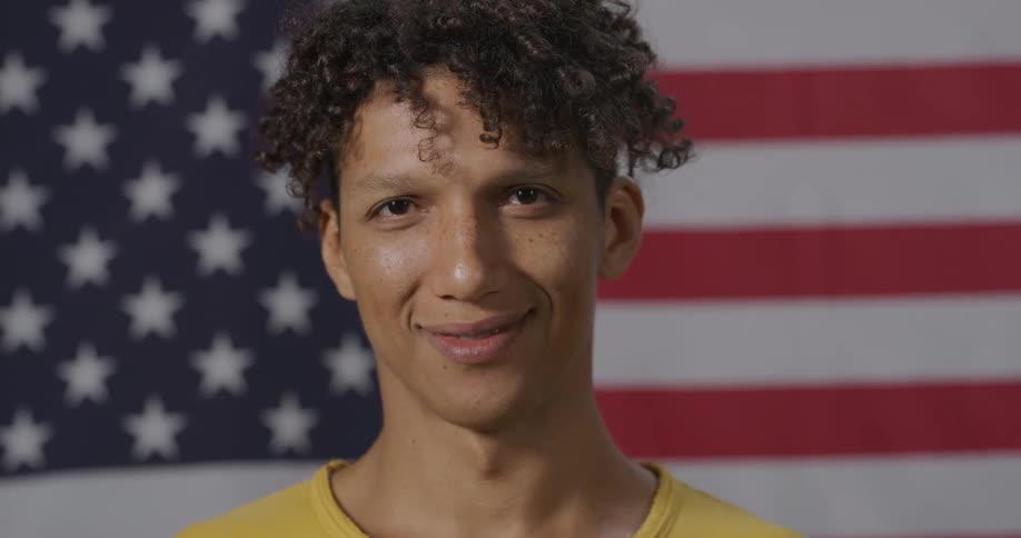 A man staring and smiling with an american flag waving in the background