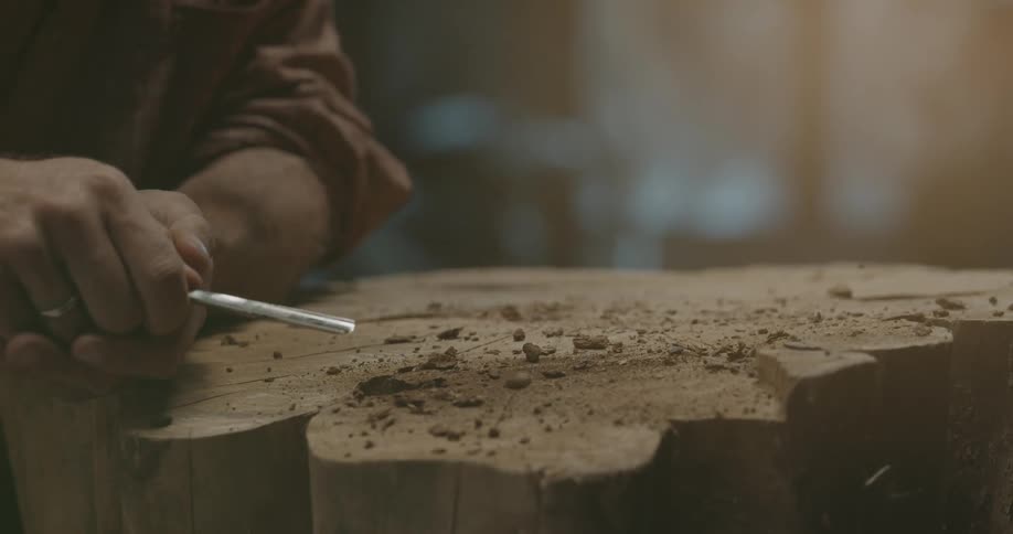 A person with a chisel sculpting a piece of wood