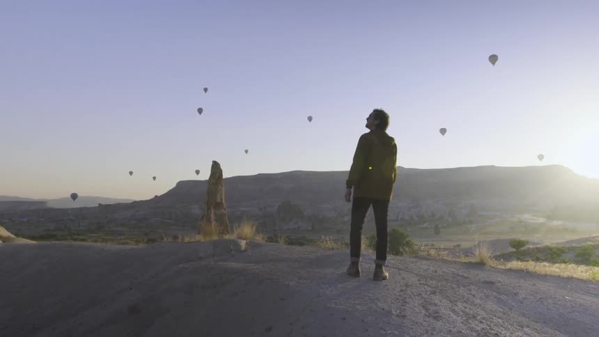 A man looks up at hot air balloons floating on a sunny day