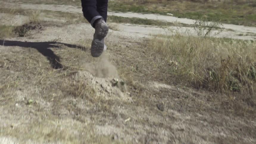 A man in a brown jacket walks on a sandy hill