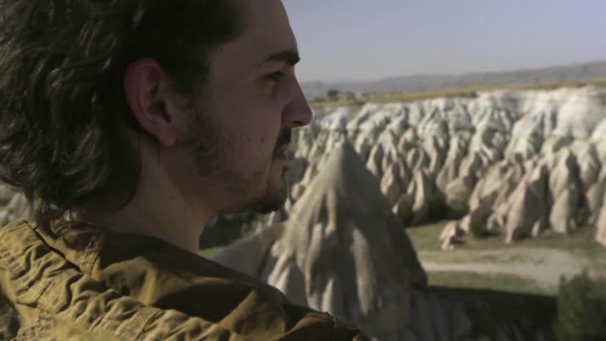 A man standing on a hillside looks over a large range of rocky hills