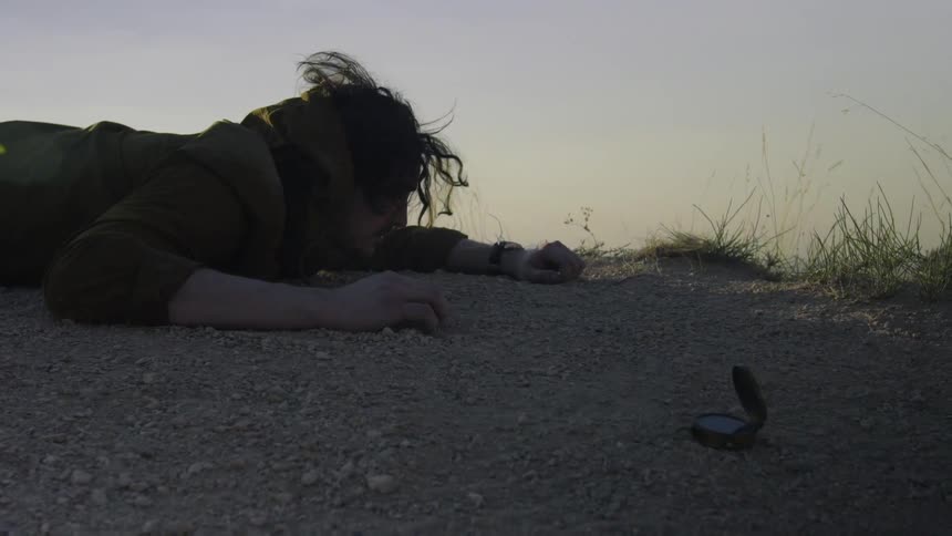 A man lies face down on the ground outside near a compass