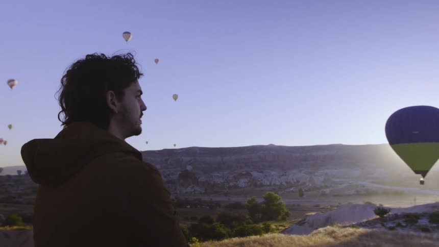 A man watches a sky filled with hot air balloons