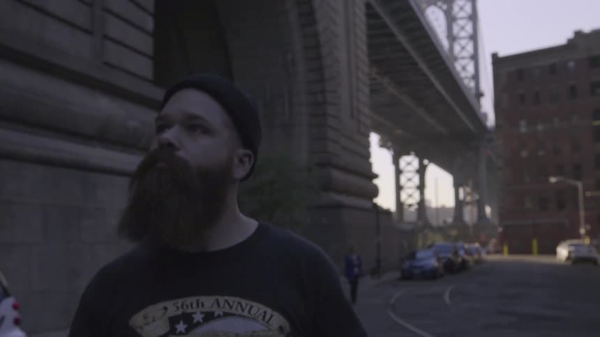 A man with a beard walks near a bridge