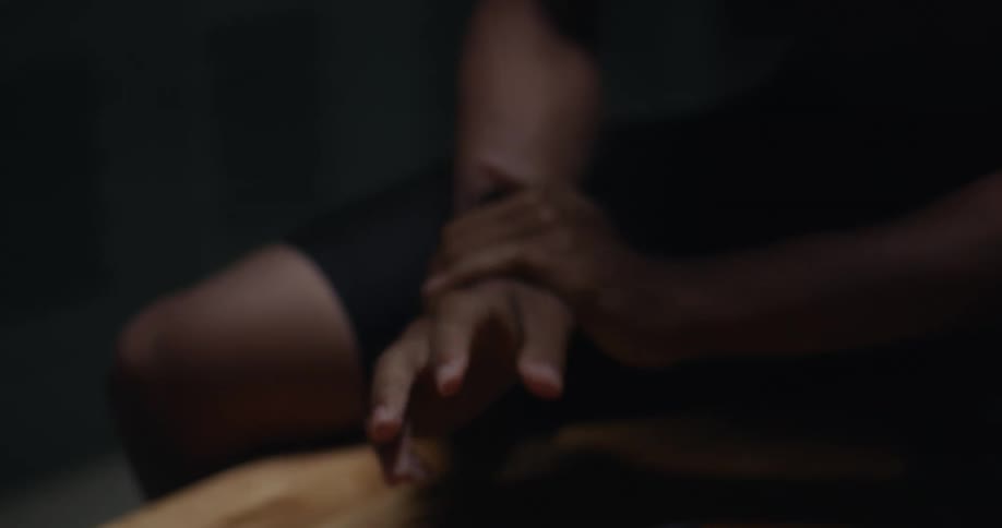 A person sitting on a bench in a locker room grasps and rolls their wrist while clasping and unclasping their hand as if to check for injury
