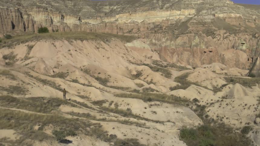 A man in a brown jacket stands in the middle of a desert hill
