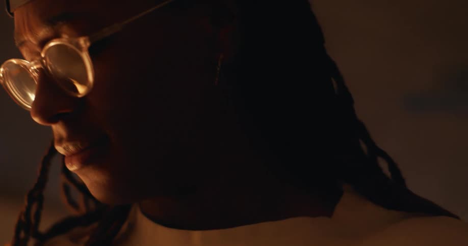 A man wearing glasses nods his head as he listens to music in a darkened room