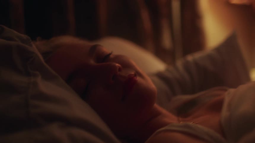 Blonde woman with a white under shirt lies in bed and smiles by looking at the camera