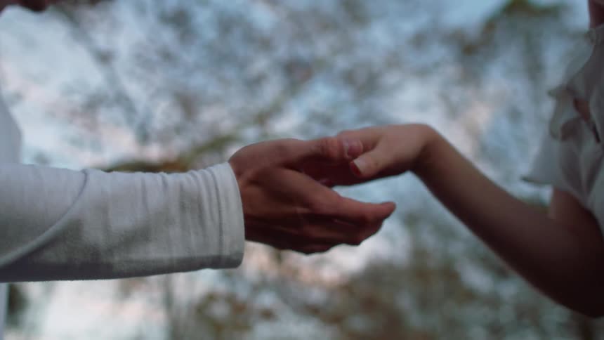 A man and woman hold their palms close to each other and move their fingers without actually touching