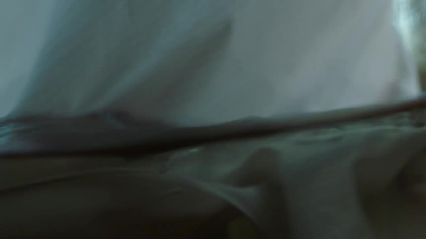A silky olive green bed sheet blows as its lined dried outdoors