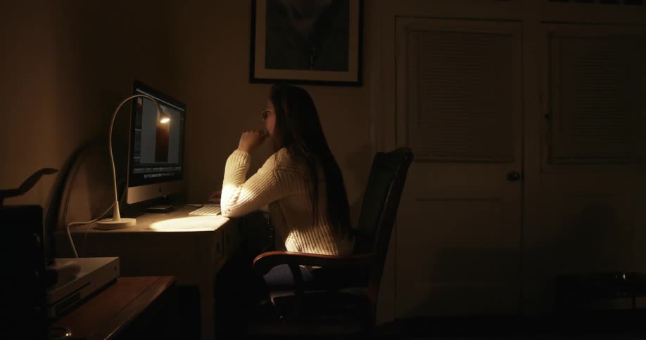 A young woman sits at a desk and concentrates on the image on her computers display