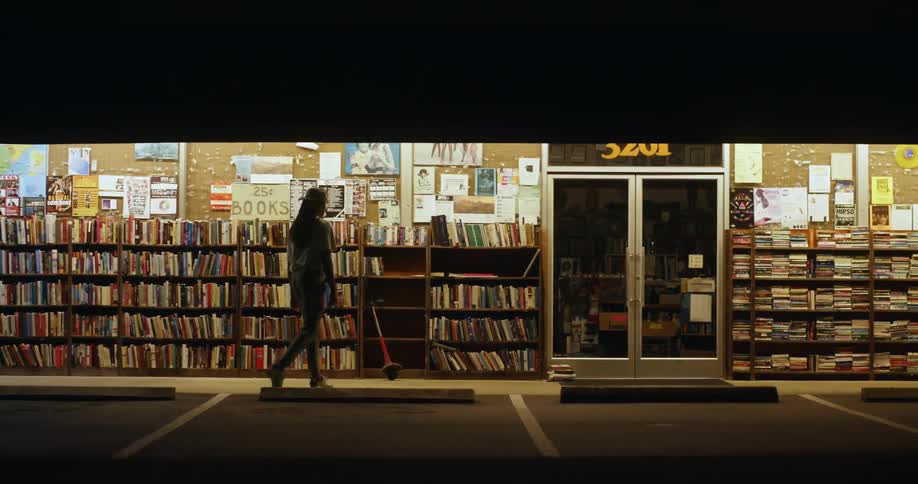 Man checks books in the bookshelves of a street bookstore at night