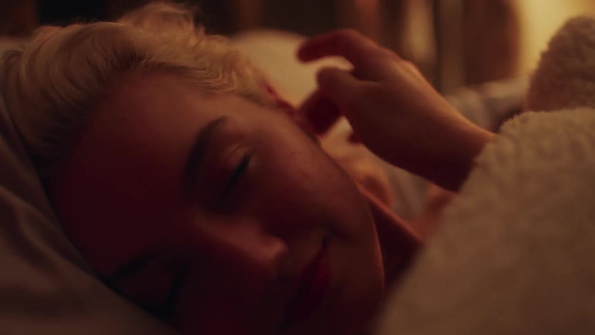 A young woman smiles into the camera while lying in a bed