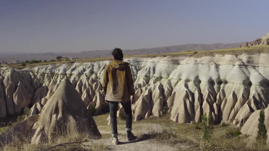 A man stands on a cliff overlooking large rocks