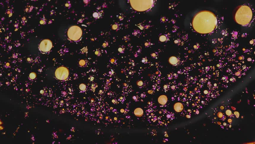 Mass containing golden particles and circles in dark purple background spreads over orange liquid