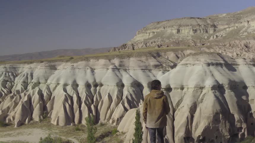 A man in a brown jacket looks out over a hilly landscape