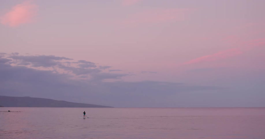 A silhouetted person paddle boarding on a lake at sunset