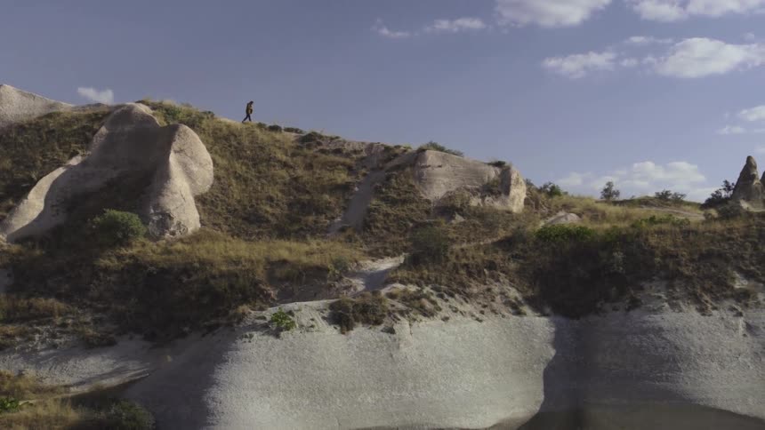 A man is walking over a large hillside covered in grass