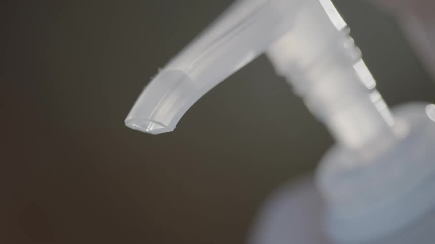 A finger pressing down on a pump bottle with hand sanitizer