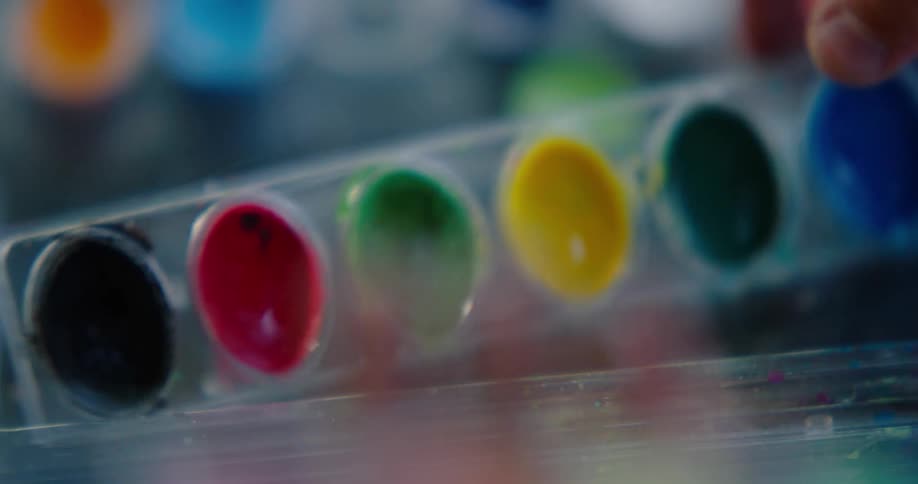 A child opens a container of multicolored water color paints and sets them on the workplace surface